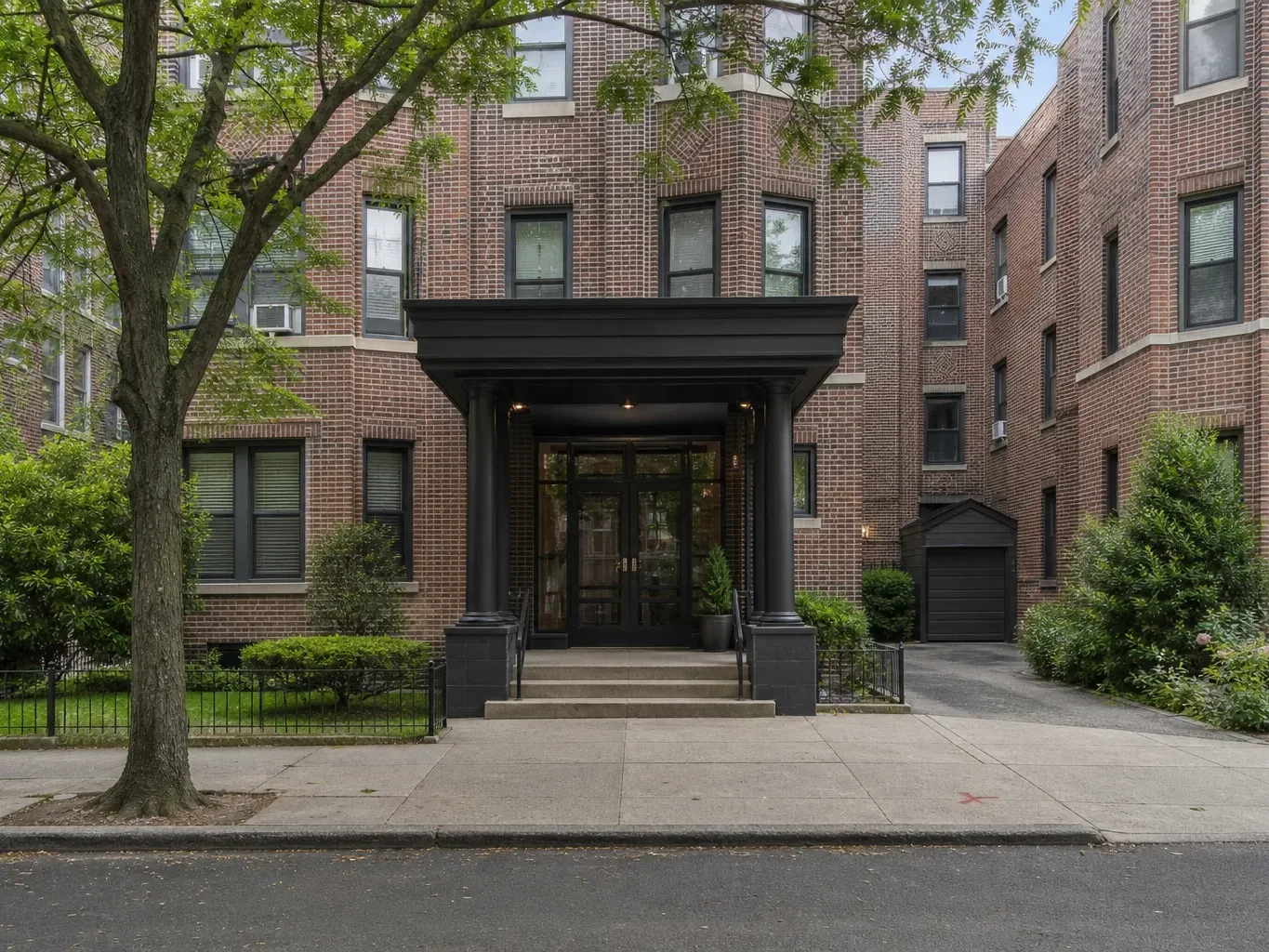 The canopied entrance of a mid-rise brick residential building on a tree-lined block